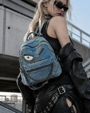 The Watcher Backpack: vivid blue denim backpack with a one-eyed monster patch, metal rivets and a chain charm